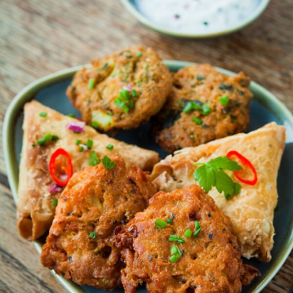 Spicy vegetable Indian snacks - pakora, samosa, onion bhaji.Indian Spicy Vegetable samosa sambusa, sambuus, samoosa, or samboksa is a fried pastry savoury filling, such as spiced potatoes, onions, peas, or lentils.Indian vegetable onion pakora with fresh raita, chili and coriander leaves. Pakora, also called pakoda, pakodi, fakkura, bhajiya, bhajji or ponako, is a fried snack. Often served as a side dish or snack.